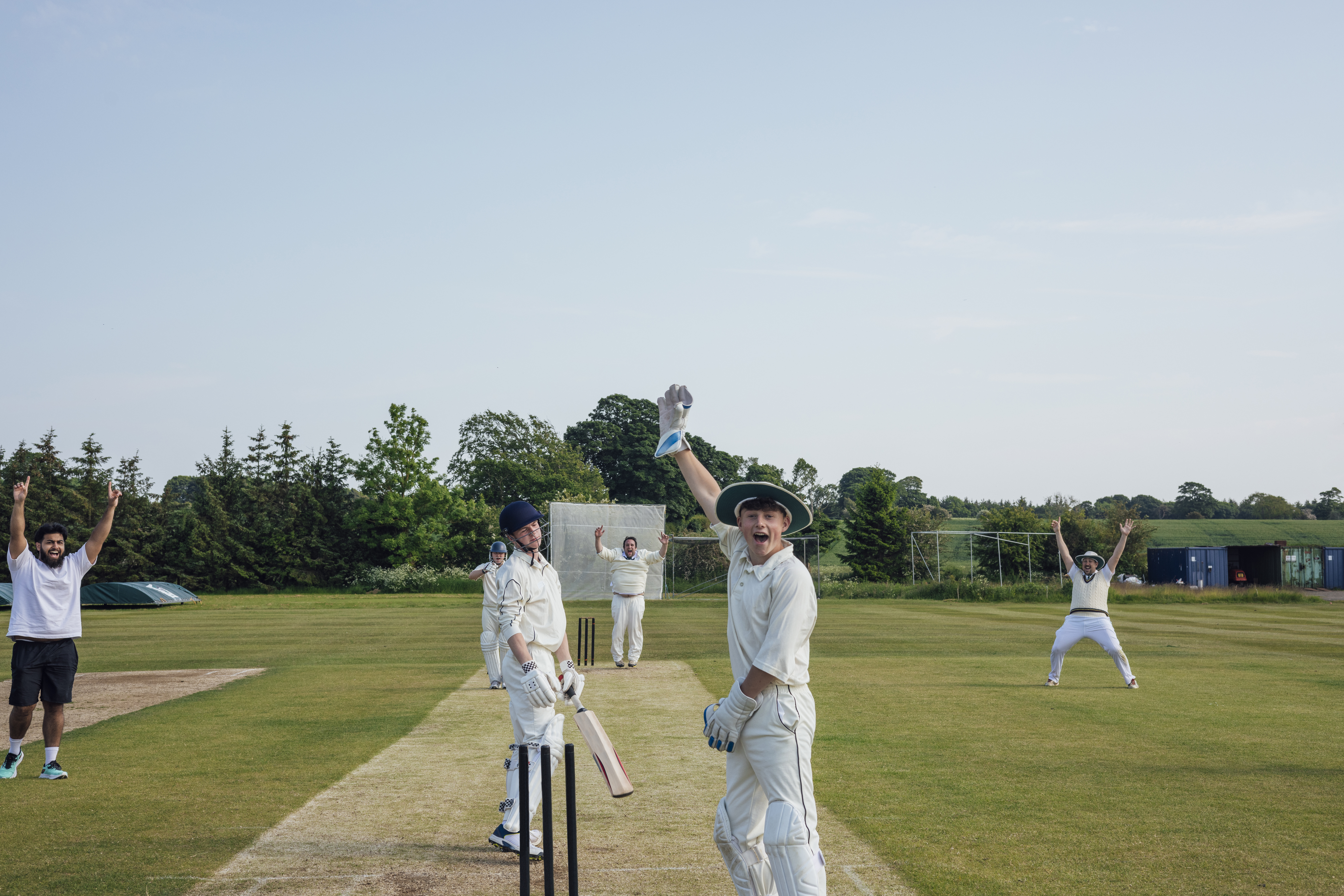 Group of young male recreational cricketers celebrating on the field after a wicket