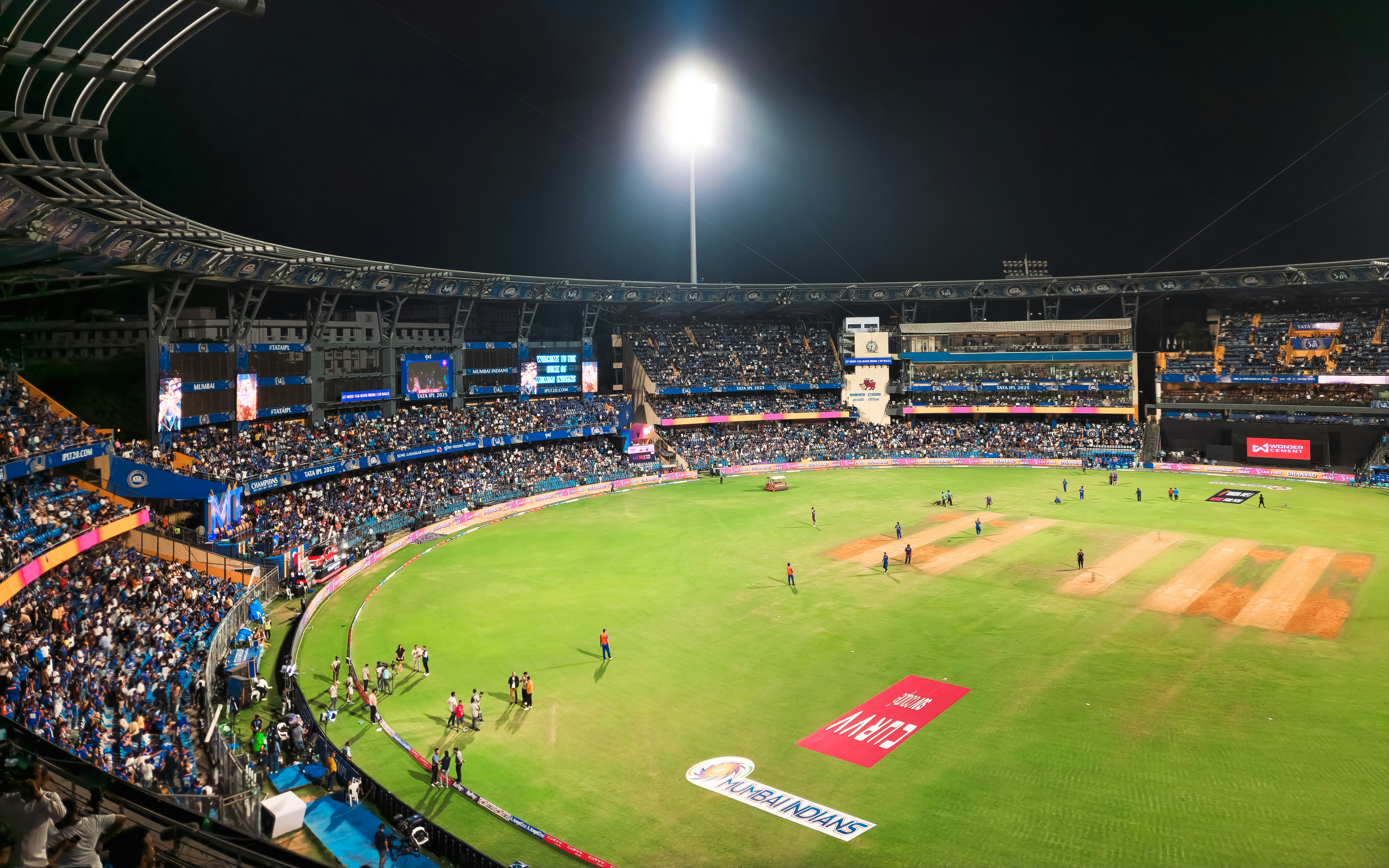 Aerial shot of large stadium and packed crowd watching a pro cricket match at night