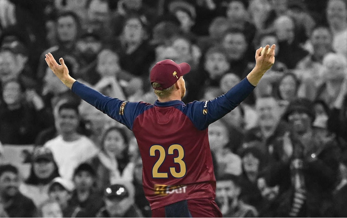 Single cricket player with back to camera and arms raised celebrating in front of crowd